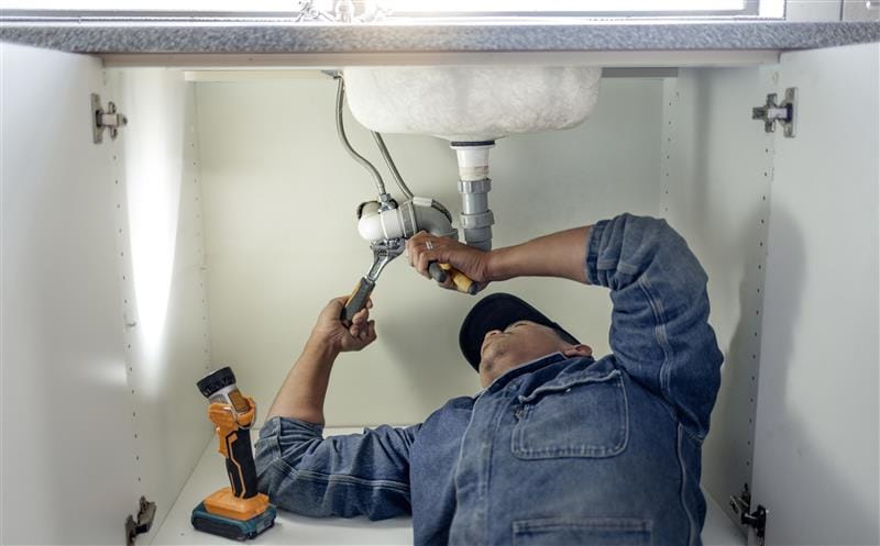 Plumber repairing pipes beneath a bathroom sink in Bullhead City