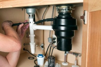 Plumber repairing a garbage disposal beneath a kitchen sink in Bullhead City