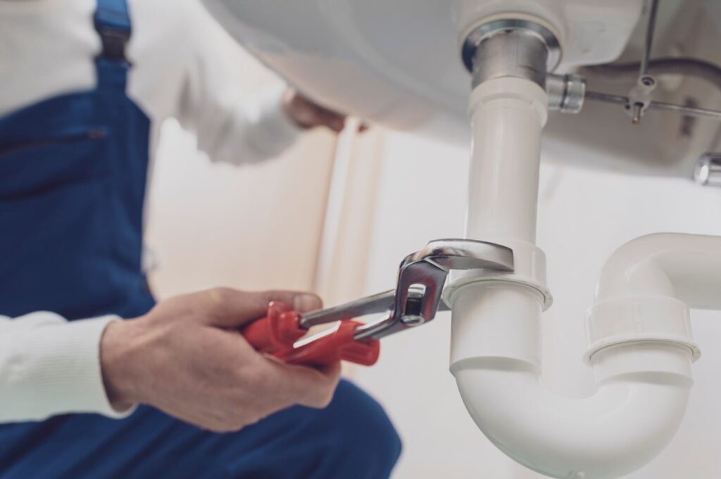 Plumber repairing a white drain pipe beneath a sink in Bullhead City