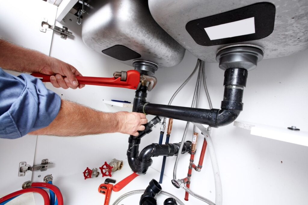Plumber repairing drain pipes beneath a kitchen sink in Bullhead City